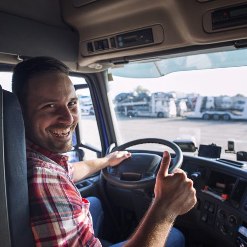 Portrait of truck driver sitting in his truck holding thumbs up.