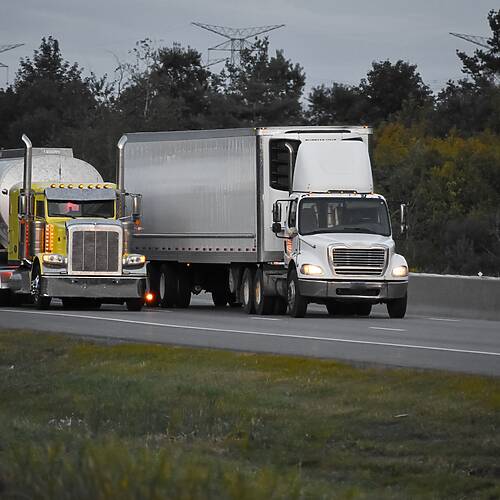 Two trailer trucks driving on the road surrounded by beautiful green trees