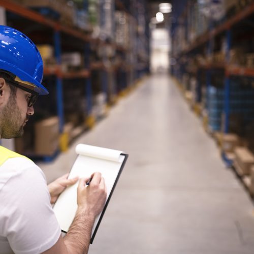 Factory worker holding clipboard and checking inventory of warehouse storage department.